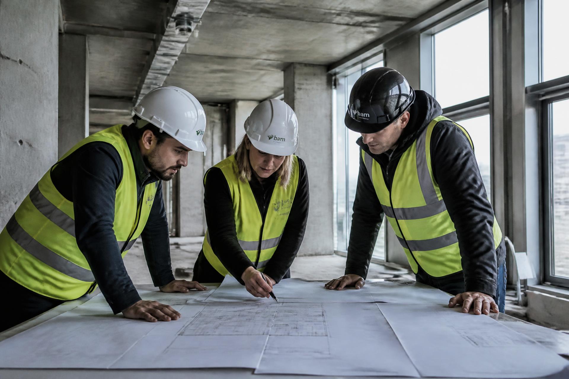 Project team in hi-vis reviewing drawings in an unfinished concrete building