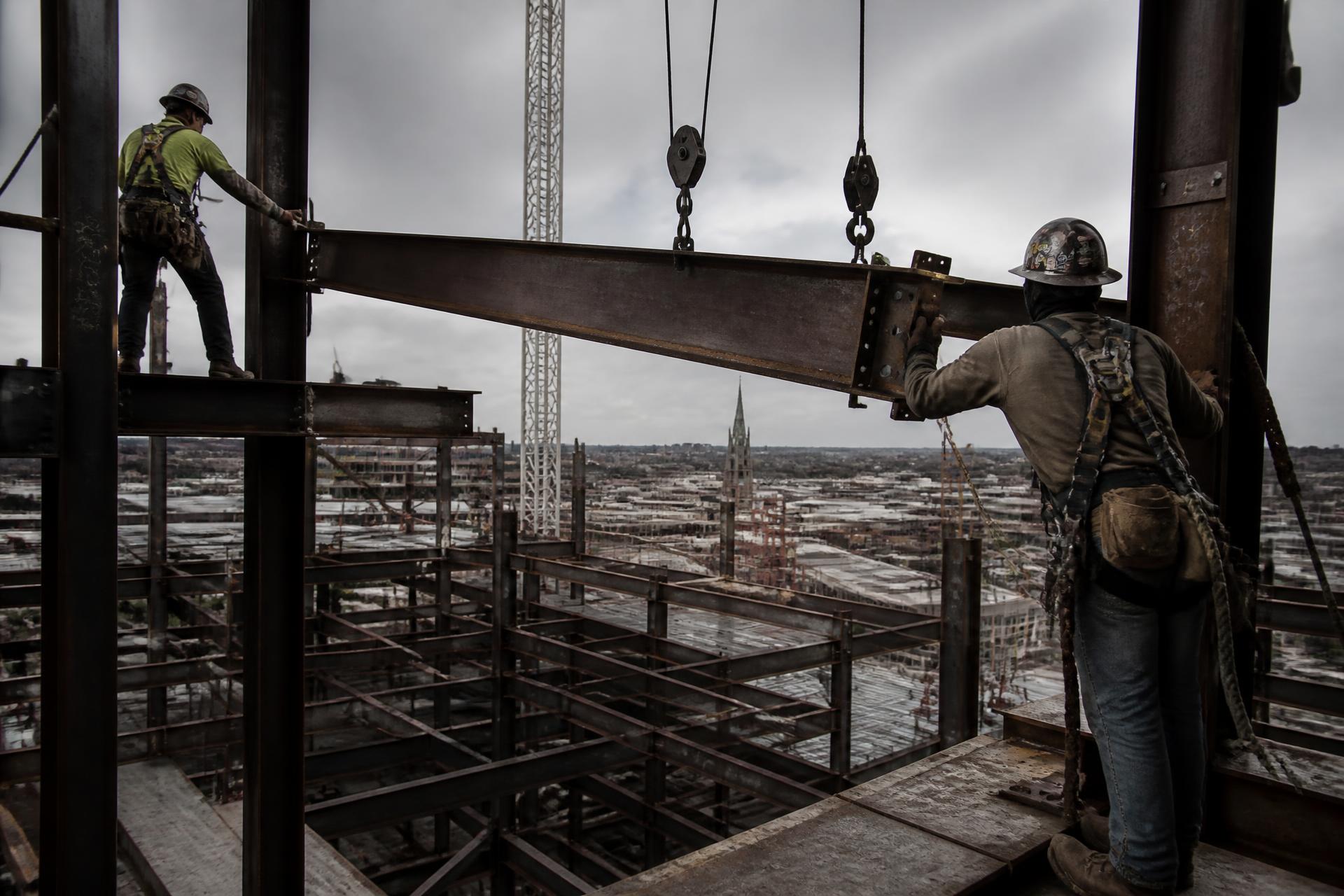 Ironworkers guiding a steel beam into place on a high-rise frame